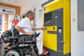 Ein Mann im Rollstuhl bedient einen Kassenautomaten